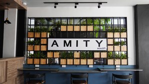 A modern bar area with a wooden and metal wall, a sign reading "AMITY," and multiple potted plants. - Amity Poshtel - Hostel (Krabi)
