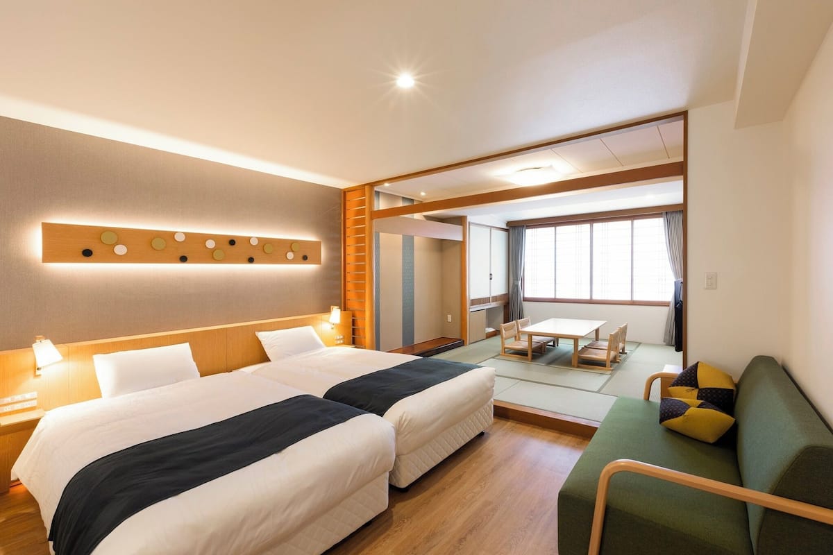 A hotel room with two beds, a sofa, a dining table, and a view of the city.