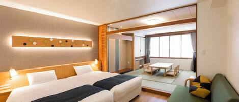 Een hotelkamer met twee bedden, een sofa, een eettafel en uitzicht op de stad.
