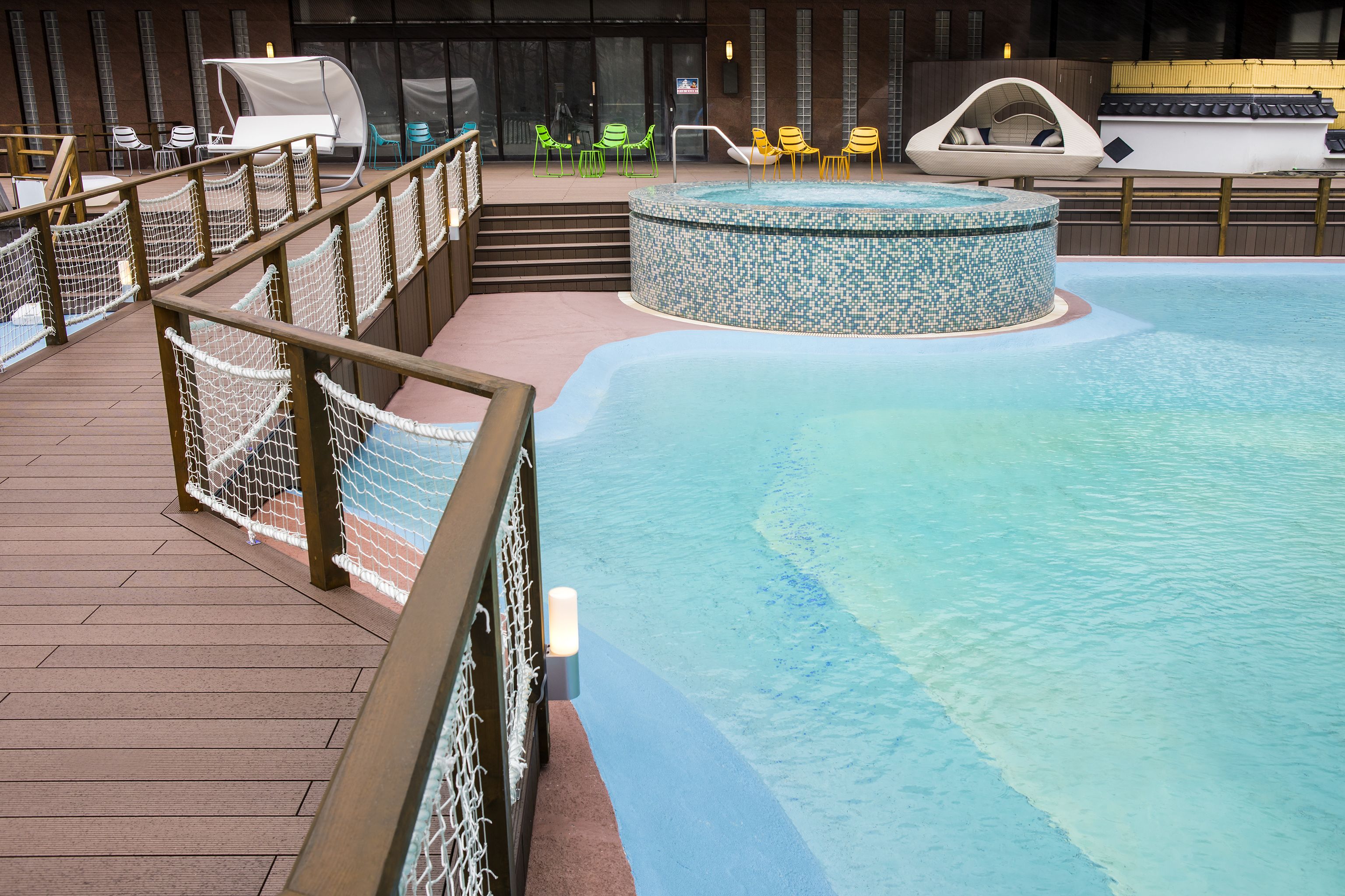 Et poolområde med jacuzzi, liggestole og en træterrasse med sikkerhedsnet.