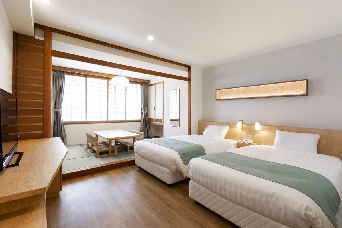 A hotel room with two beds, a desk, and a TV.