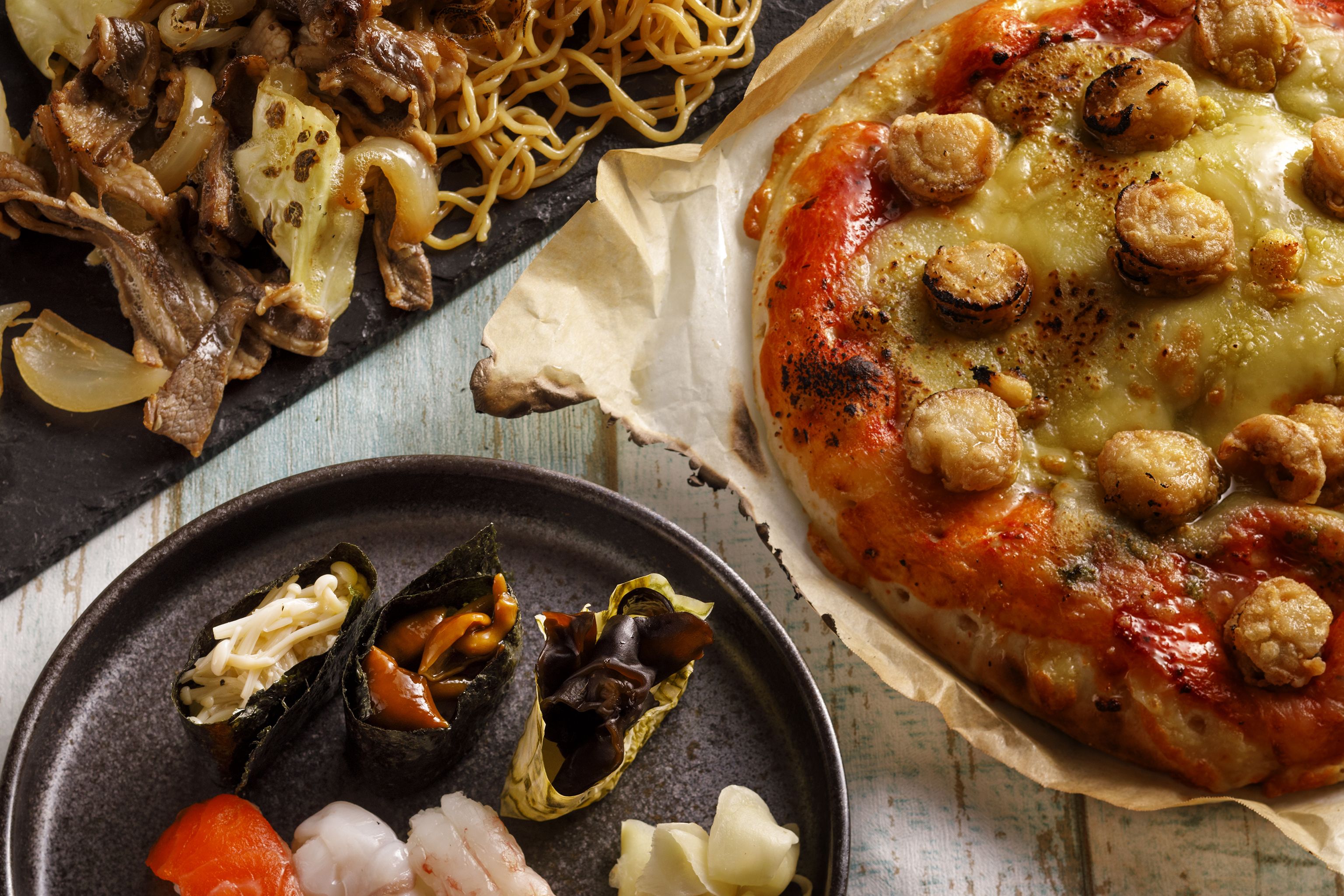 A variety of dishes including a pizza with cheese and mushrooms, a plate with seafood, and noodles with meat.