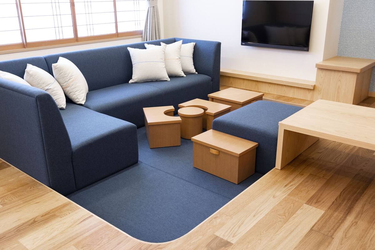 A modern living room with a blue sofa, wooden side tables, and a flat-screen TV mounted on the wall.