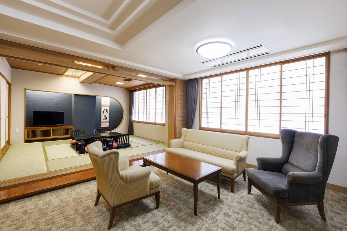 A traditional Japanese-style room with tatami flooring, a low wooden table, a sofa, and a chair.