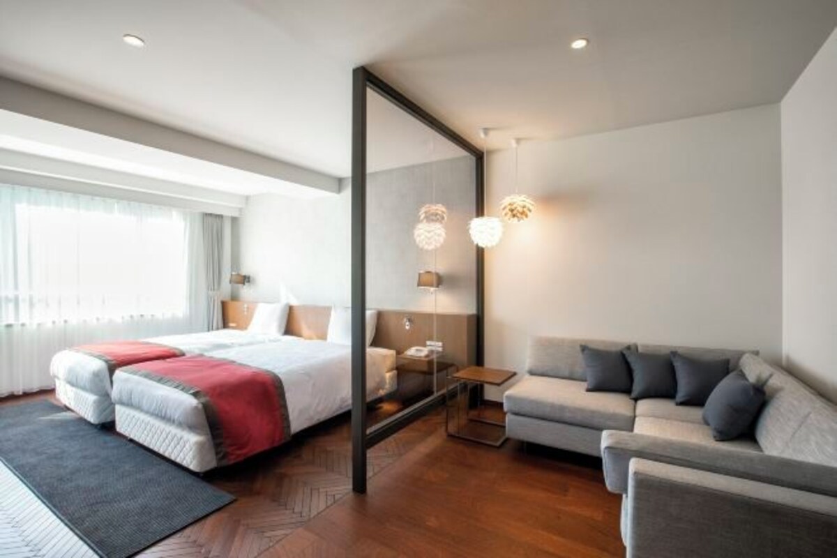 A modern hotel room with a bed, a sofa, a small table, and a mirror.
