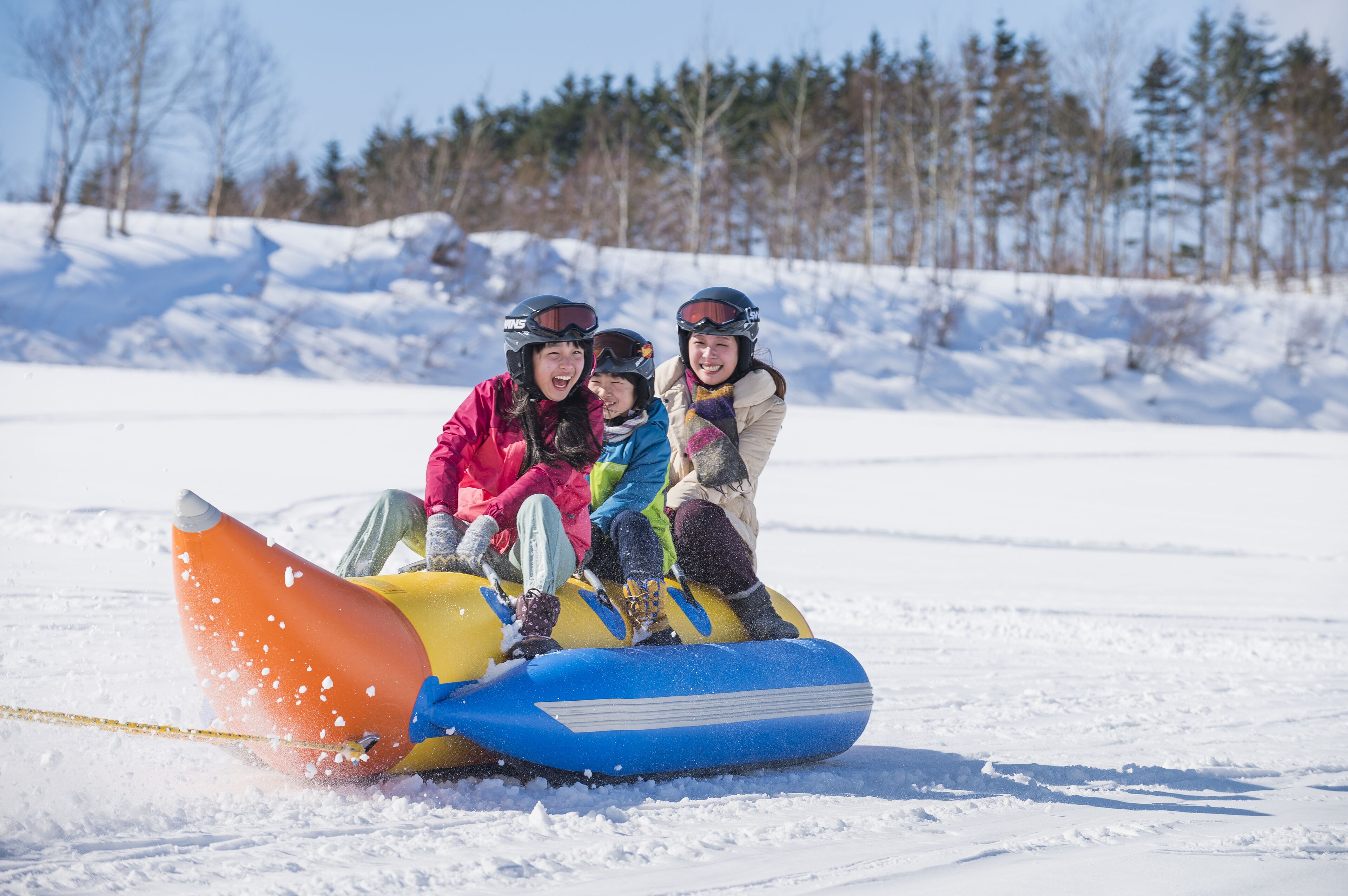 Three people on a snow tube in a snowy landscape.