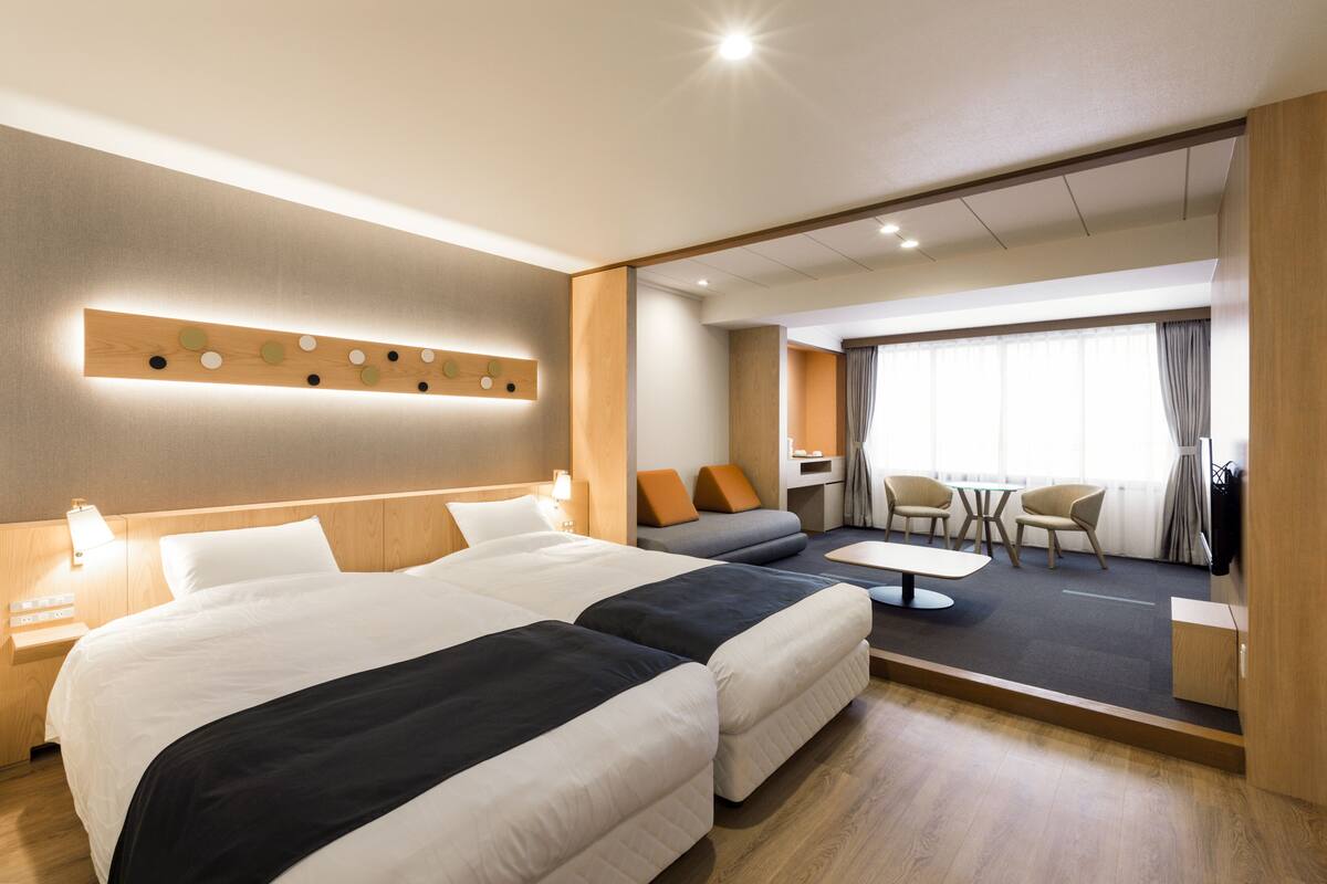 A hotel room with two beds, a sofa, a dining table, and a TV.