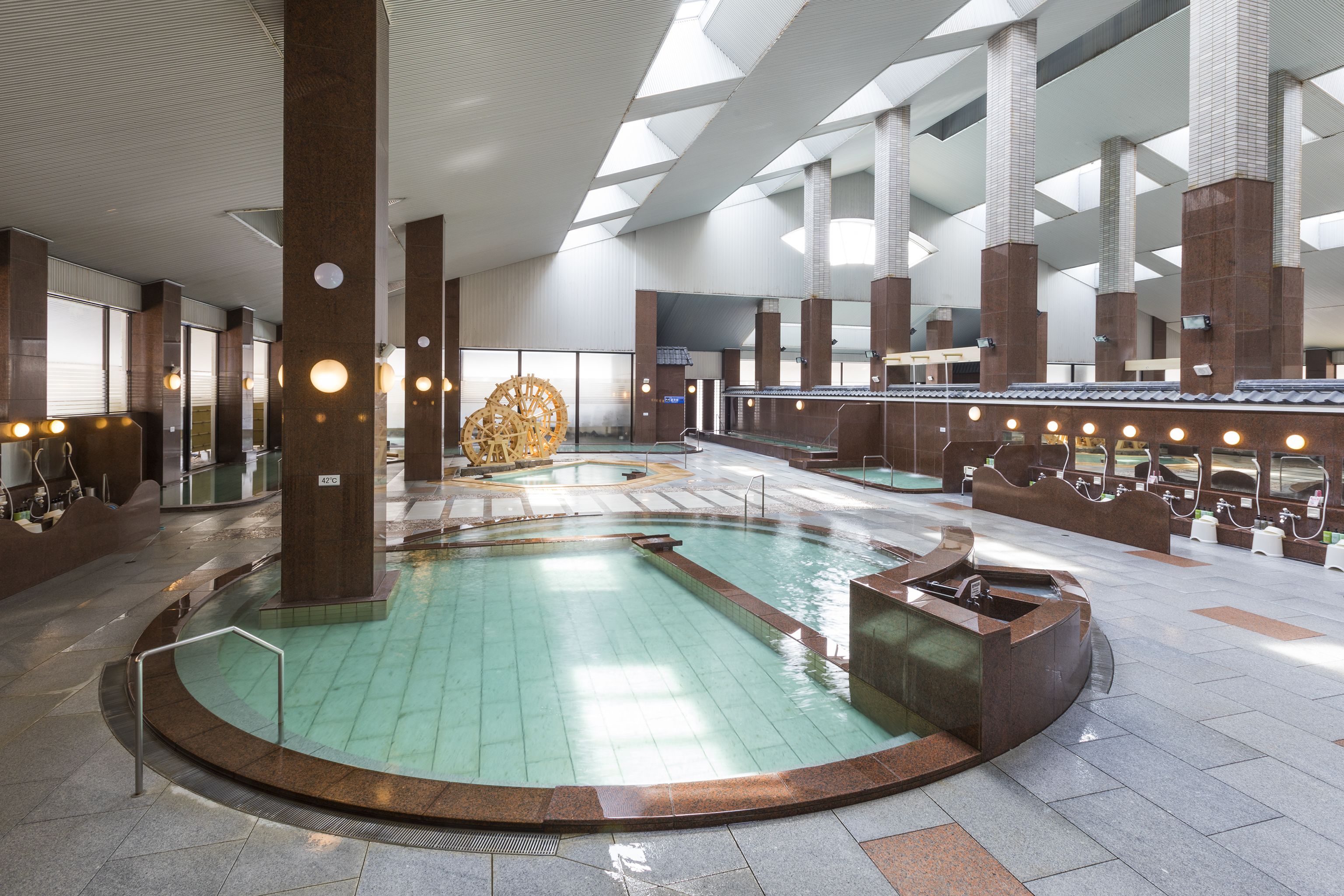 An indoor swimming pool with a central fountain, surrounded by large pillars and a high ceiling with skylights.