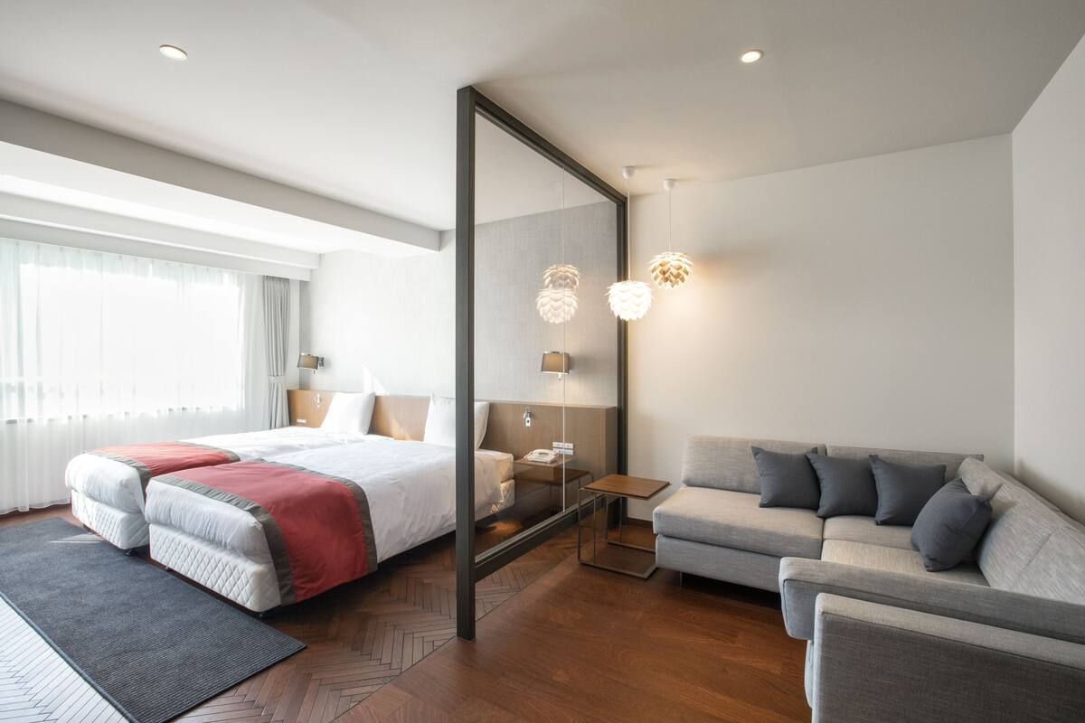 A modern hotel room with a large bed, a sofa, a desk, and a mirror.