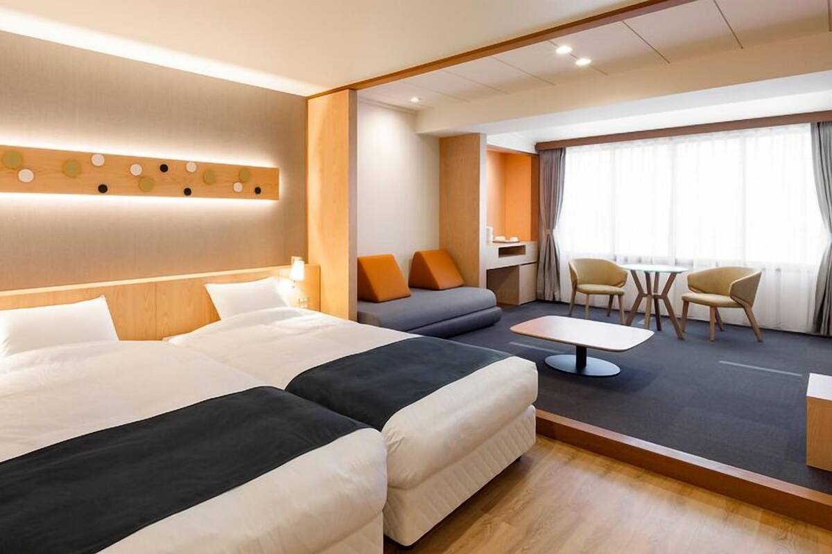 A hotel room with a large bed, a sofa, a small table, and a seating area with chairs.