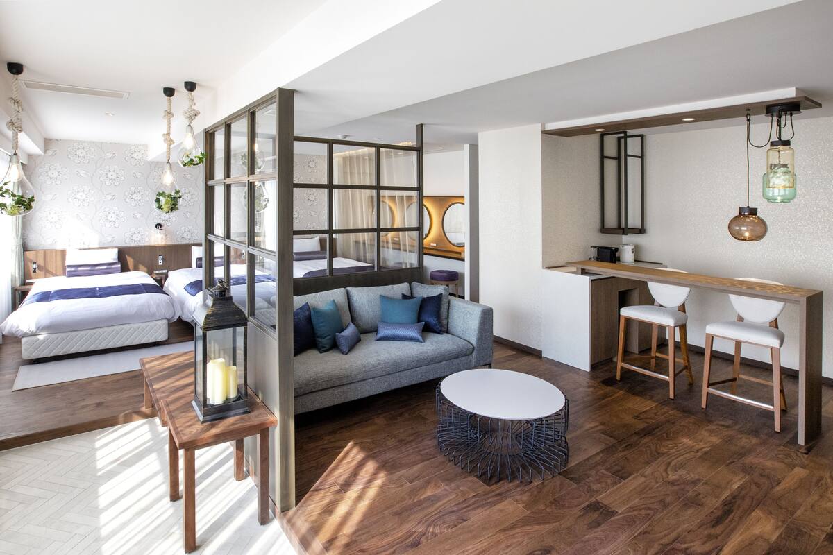 A modern hotel room with a sofa, a round table, a desk with two chairs, a bed, and a large mirror.