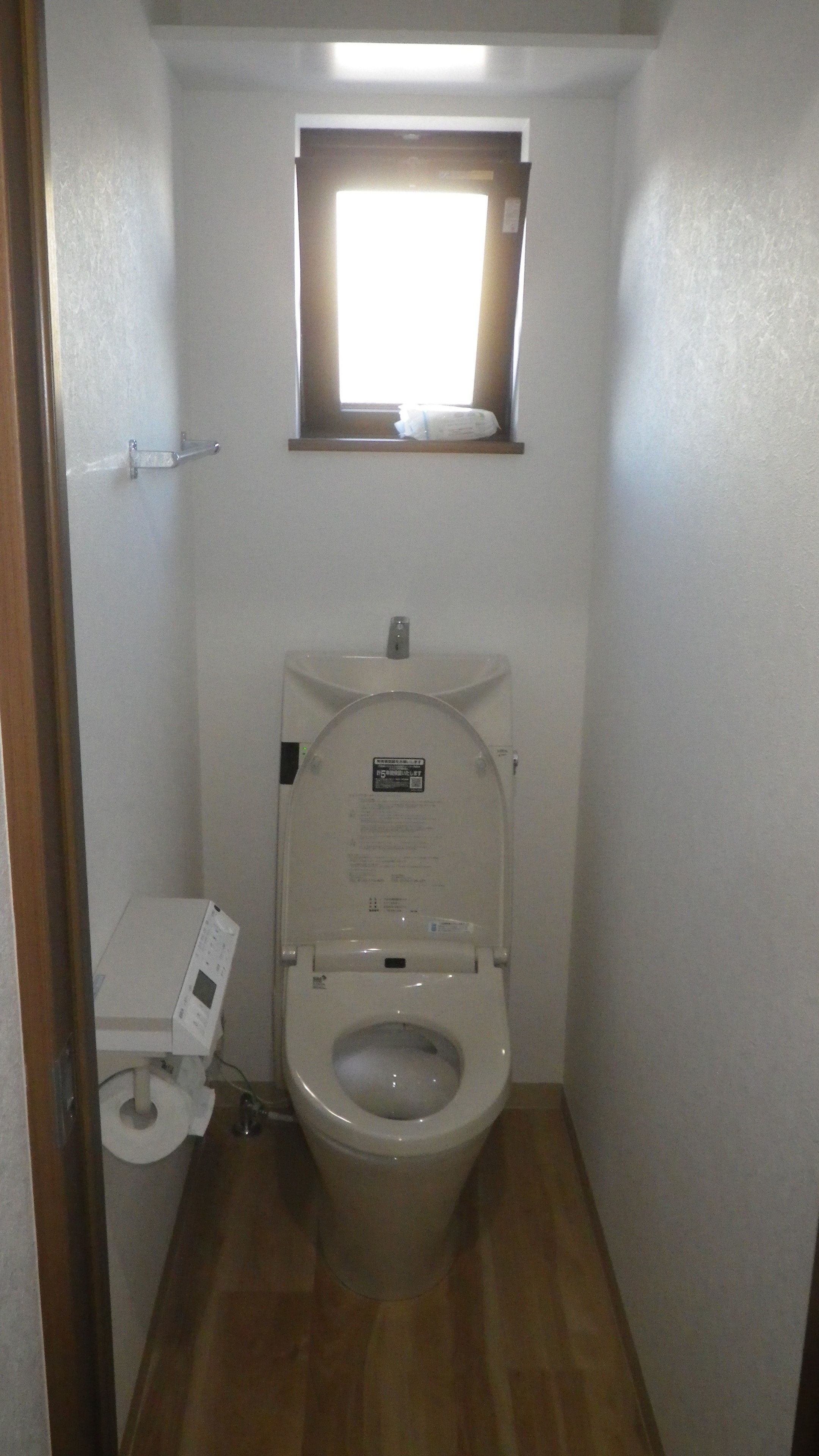 A small, compact bathroom with a toilet, a window, and a shelf.