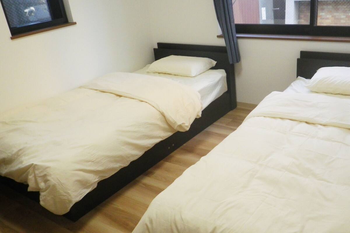 Two single beds with white bedding in a room with wooden flooring and a window.