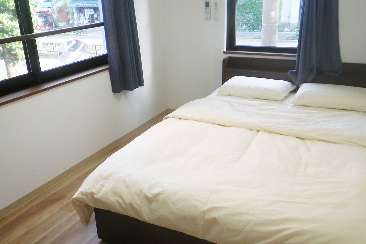 A bedroom with a bed, a window, and a thermostat on the wall.