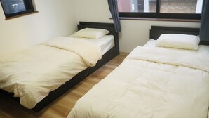 Two single beds with white bedding in a room with wooden flooring and a window with curtains. - Nagomi (Itabashi)