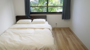 A bedroom with a bed, a window with curtains, and a wooden floor. - Nagomi (Itabashi)