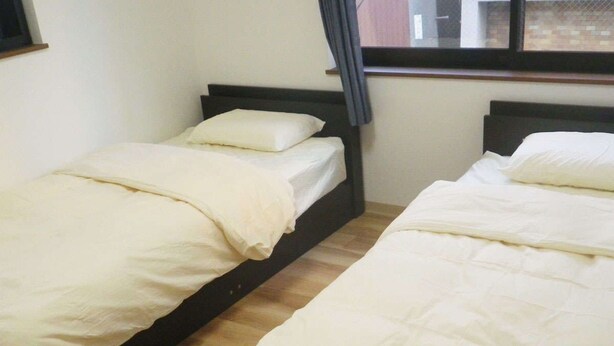 Two single beds with white bedding in a room with wooden flooring and a window with curtains. - Nagomi (Itabashi)