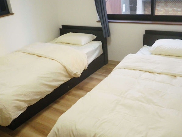 Two single beds with white bedding in a room with wooden flooring and a window with curtains. - Nagomi (Itabashi)