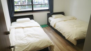 A small room with two beds, a window, and a wooden floor. - Nagomi (Itabashi)
