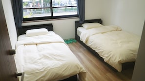 A small room with two beds, a window, and a wooden floor. - Nagomi (Itabashi)