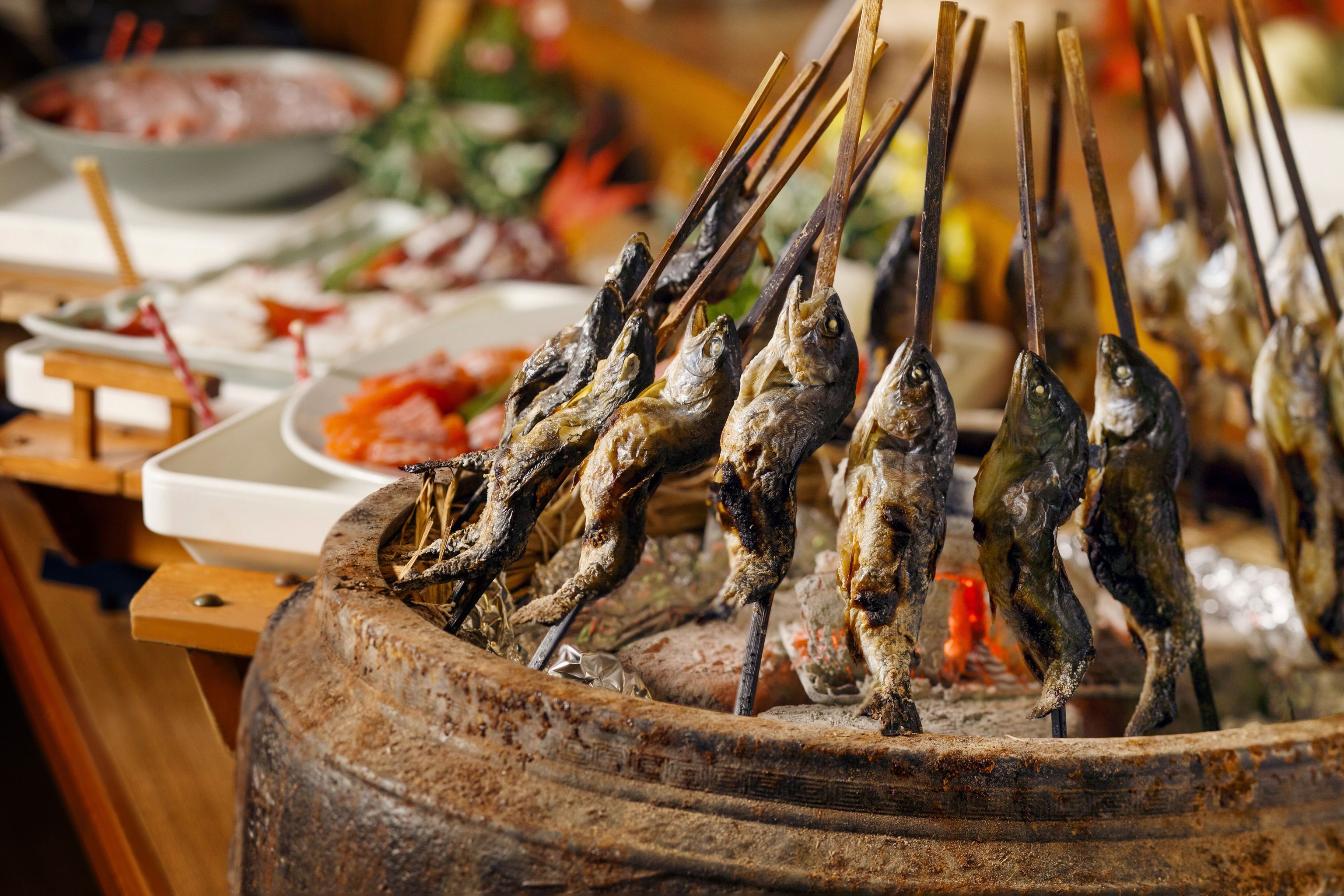 A variety of grilled fish on skewers, displayed in a rustic, round metal container.
