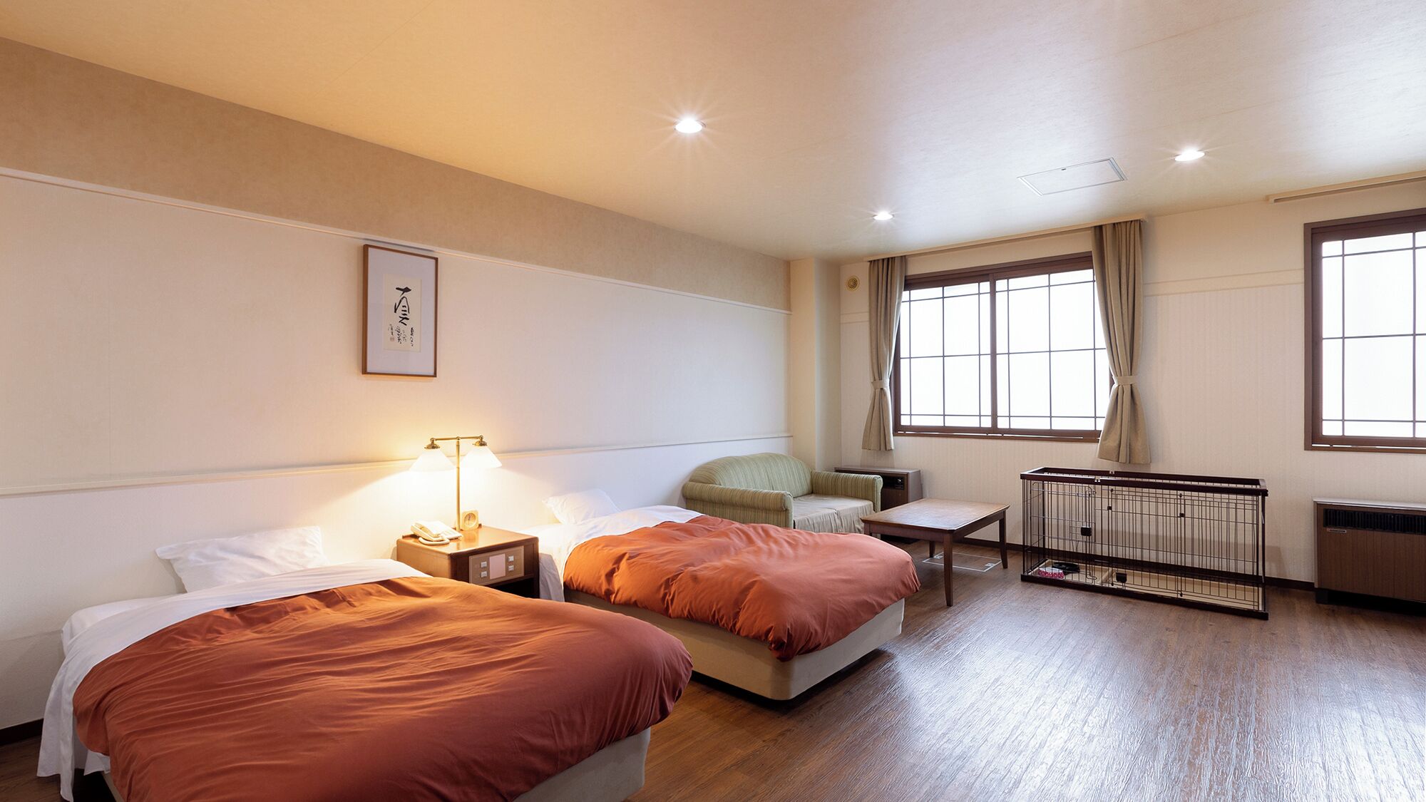 Une chambre d’hôtel avec deux lits, une petite table, une chaise, un radiateur et une fenêtre avec des rideaux.