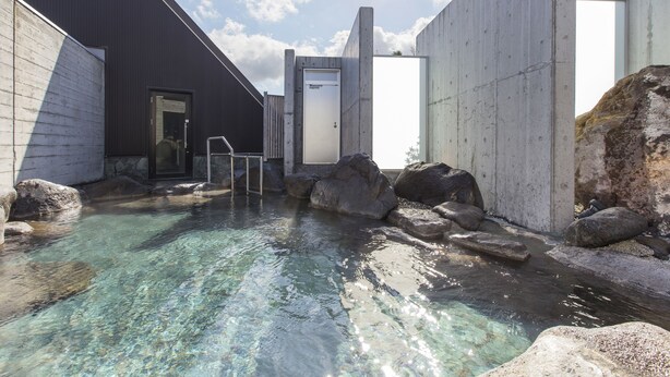 A clear outdoor pool area with rocks, a wooden deck, and a building with a door and windows. - Horohoro Sanso (Date)