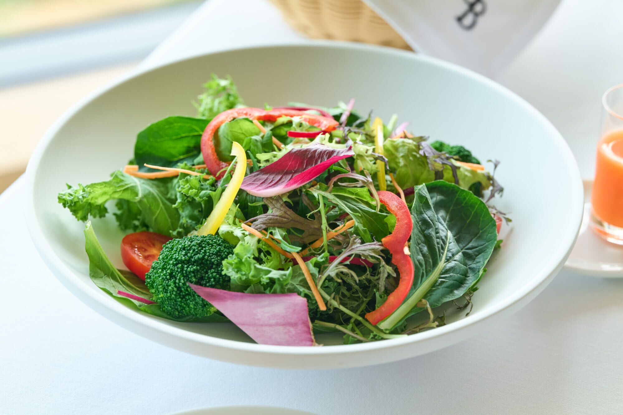 A bowl of mixed greens salad with various vegetables like broccoli, red onions, and leafy greens.