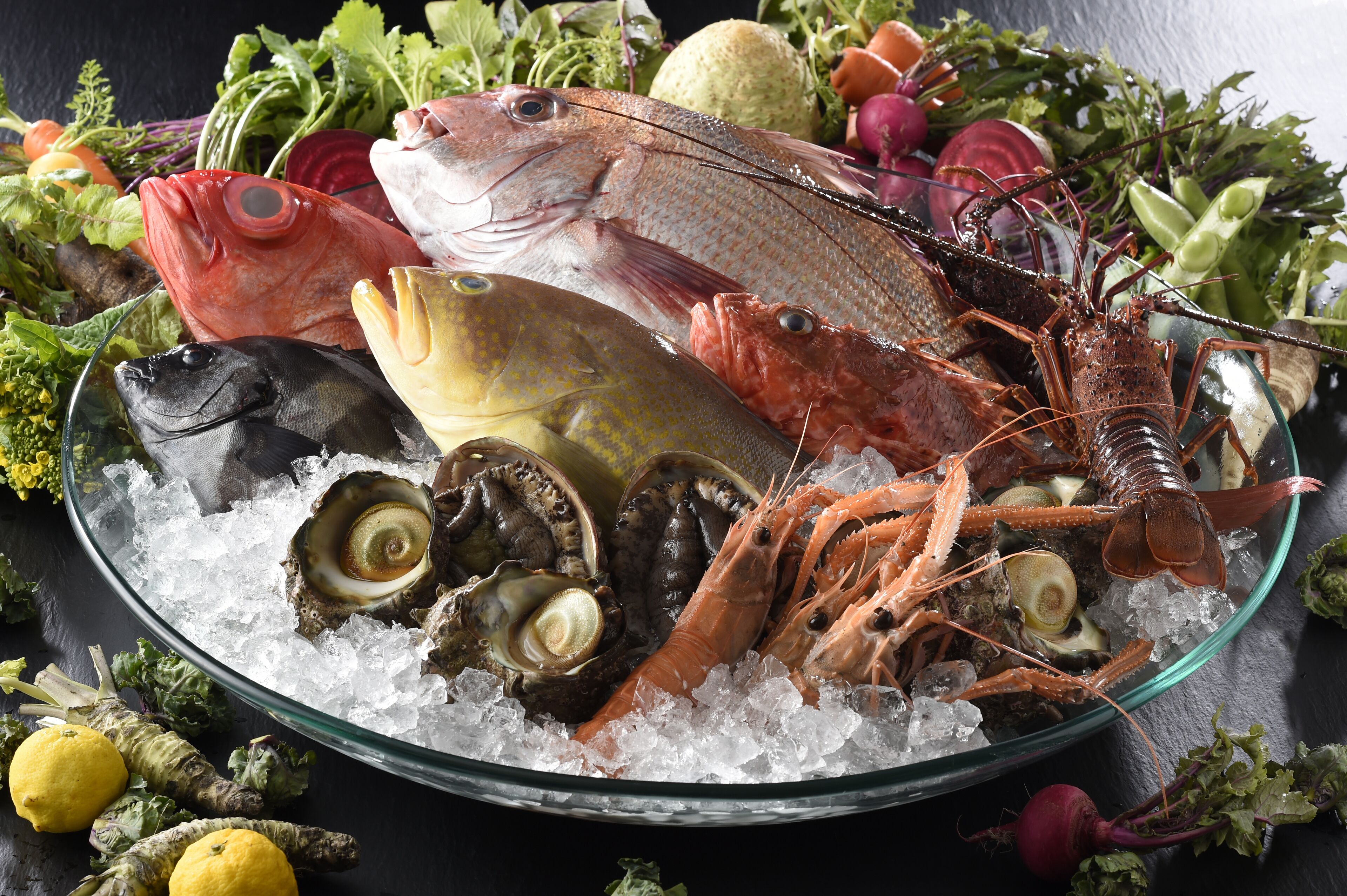 A variety of seafood including fish, shrimp, and oysters on ice, surrounded by vegetables and herbs.