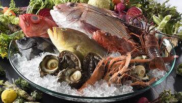 A variety of seafood including fish, shrimp, and oysters on ice, surrounded by vegetables and herbs.