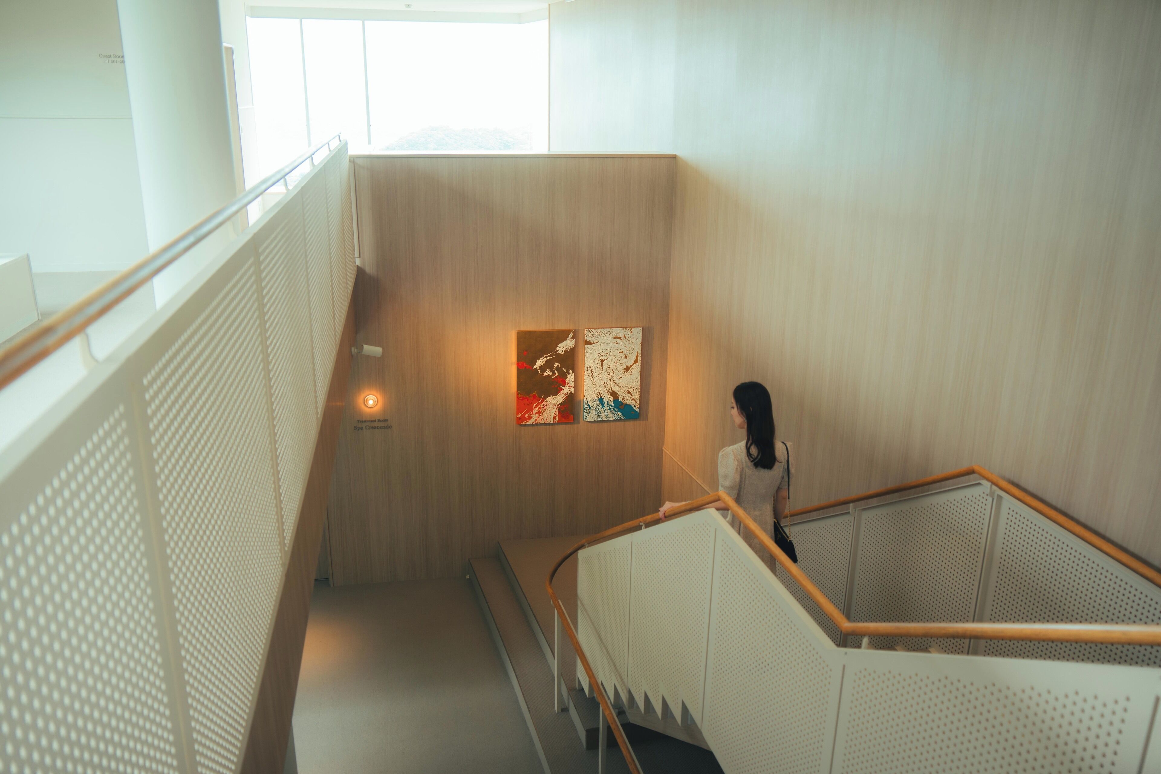 A modern interior with a wooden staircase, a white railing, and a wall-mounted artwork.