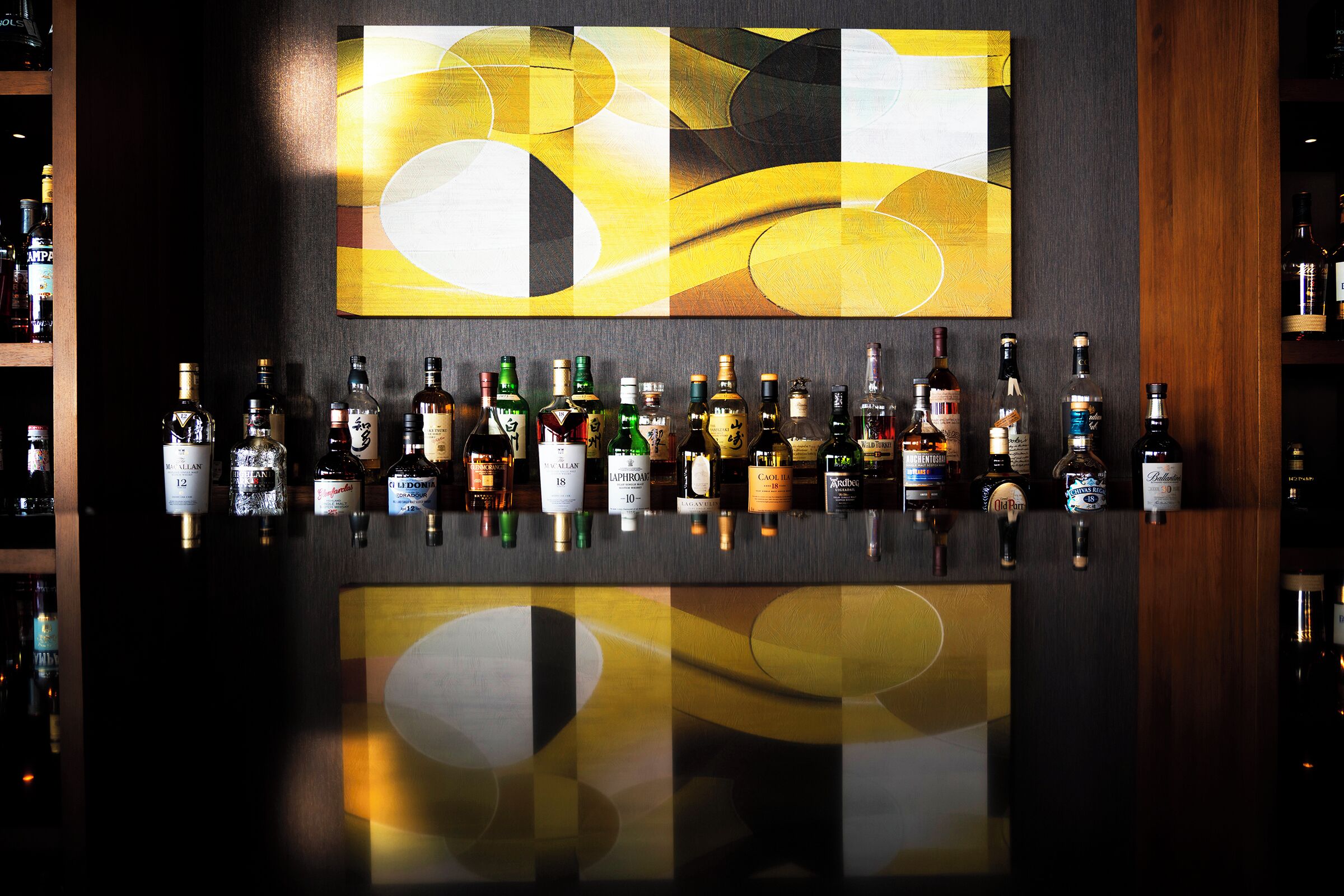 A bar with various liquor bottles and a large abstract painting on the wall.