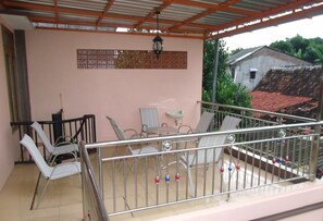 Un balcón techado con barandillas metálicas, una mesa, sillas y un panel decorativo en la pared.