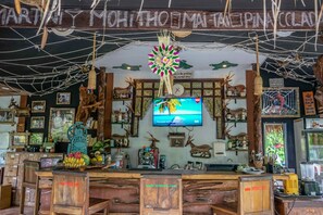 A bar with wooden furniture, a television, and various decorations including antlers and a large flower. - KTS Balinese Villas (Dalung)