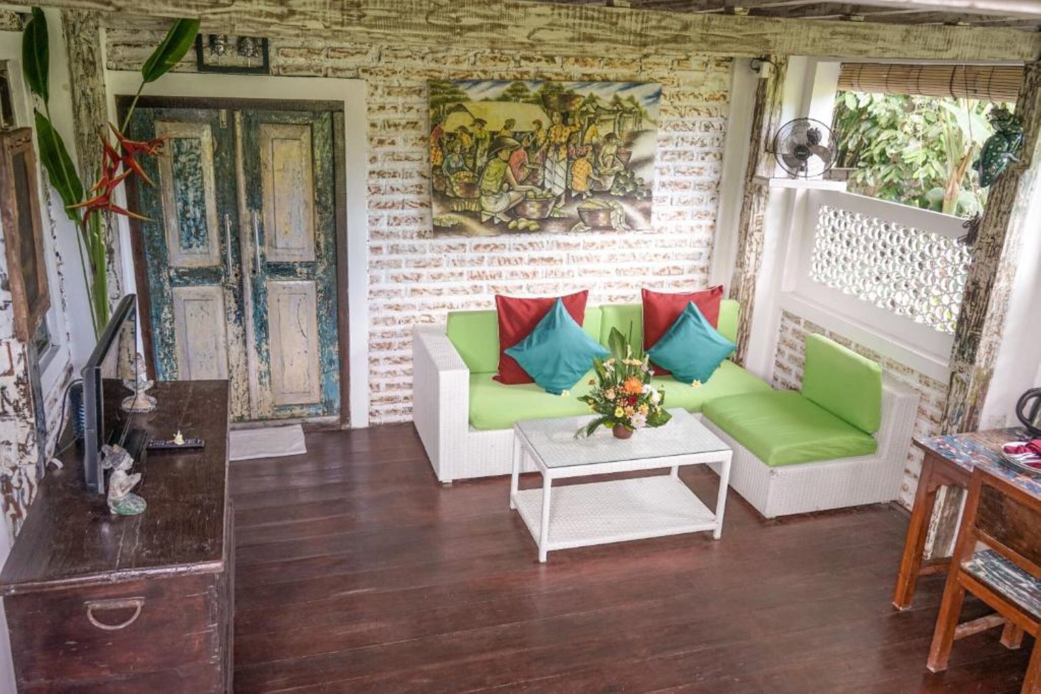Un salon avec un canapé blanc, des coussins verts, une table basse et une tapisserie murale.