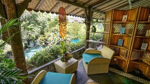 Un rincón acogedor al aire libre con mobiliario de mimbre y vistas a un exuberante jardín y una piscina.