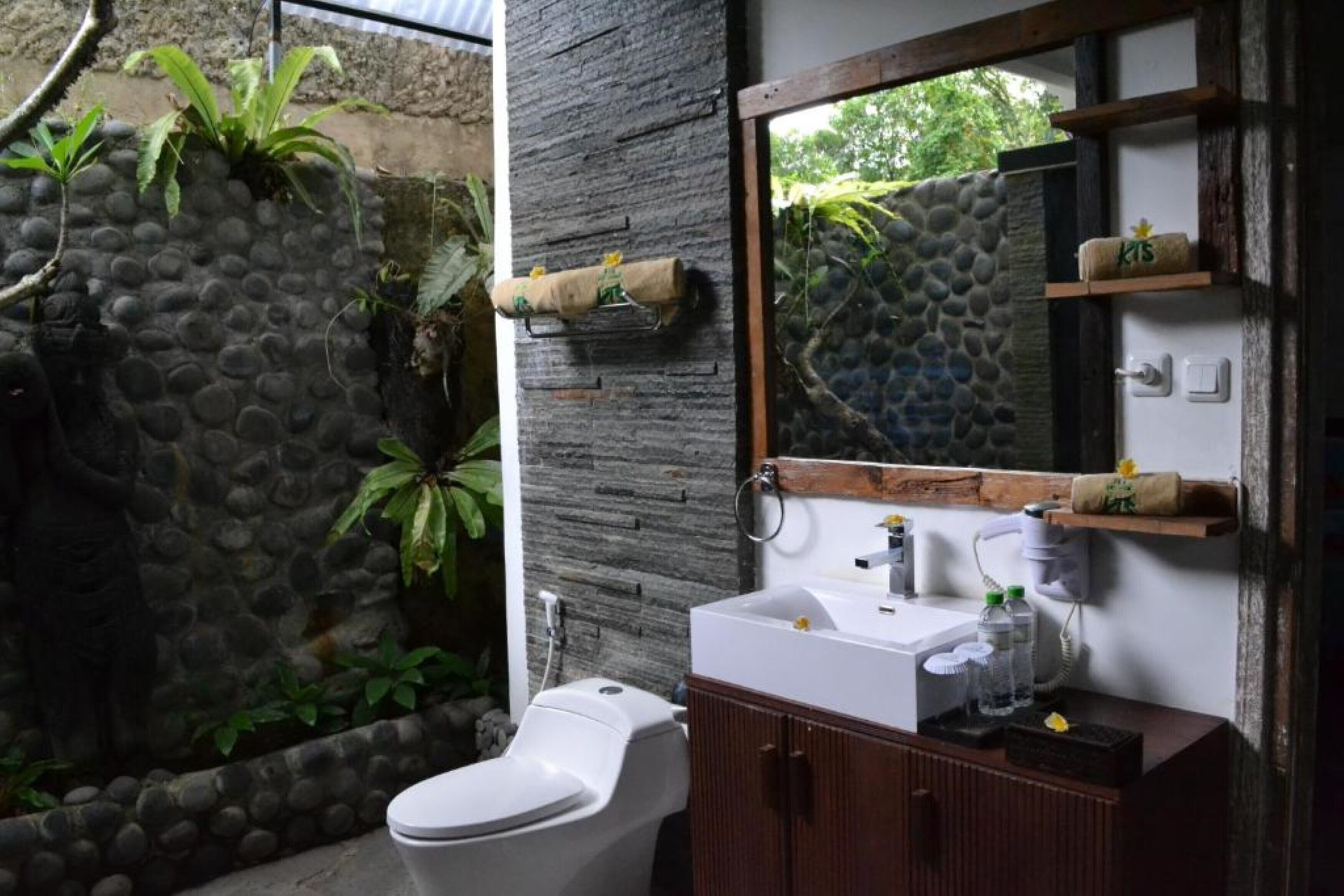 A bathroom with a stone wall, a toilet, a wooden cabinet, and a mirror.