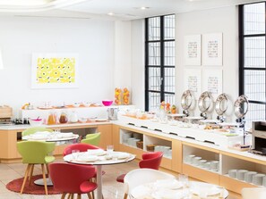 A bright, modern dining area with colorful chairs, a long buffet table, and large windows.