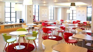 A modern dining area with round tables and chairs in various colors, a counter with a cash register, and artwork on the walls. - Sakaide Plaza Hotel (Sakaide)