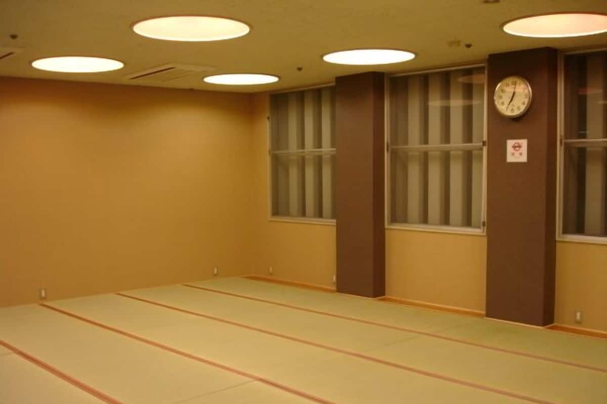 Una habitación con esteras de tatami, un reloj y una ventana con persianas.