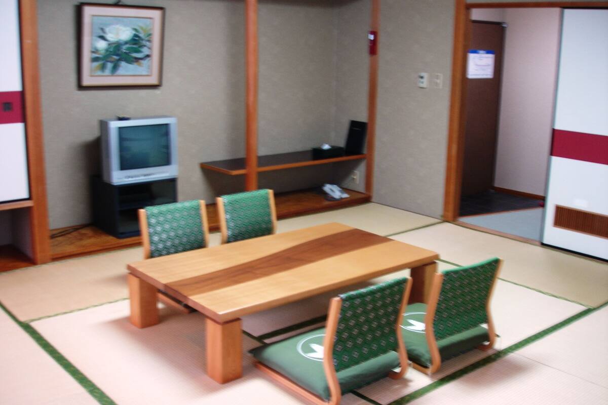 Una habitación de estilo japonés tradicional con suelo de tatami, una mesa de madera baja y sillas con cojines verdes.