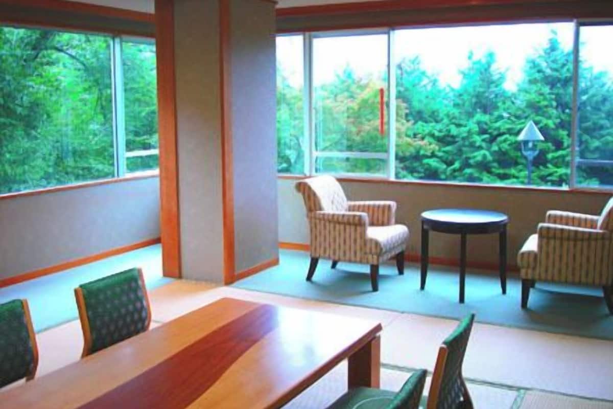 Una habitación con una mesa y sillas de madera, ventanas amplias con vistas a la vegetación y una pequeña mesa redonda con sillas.