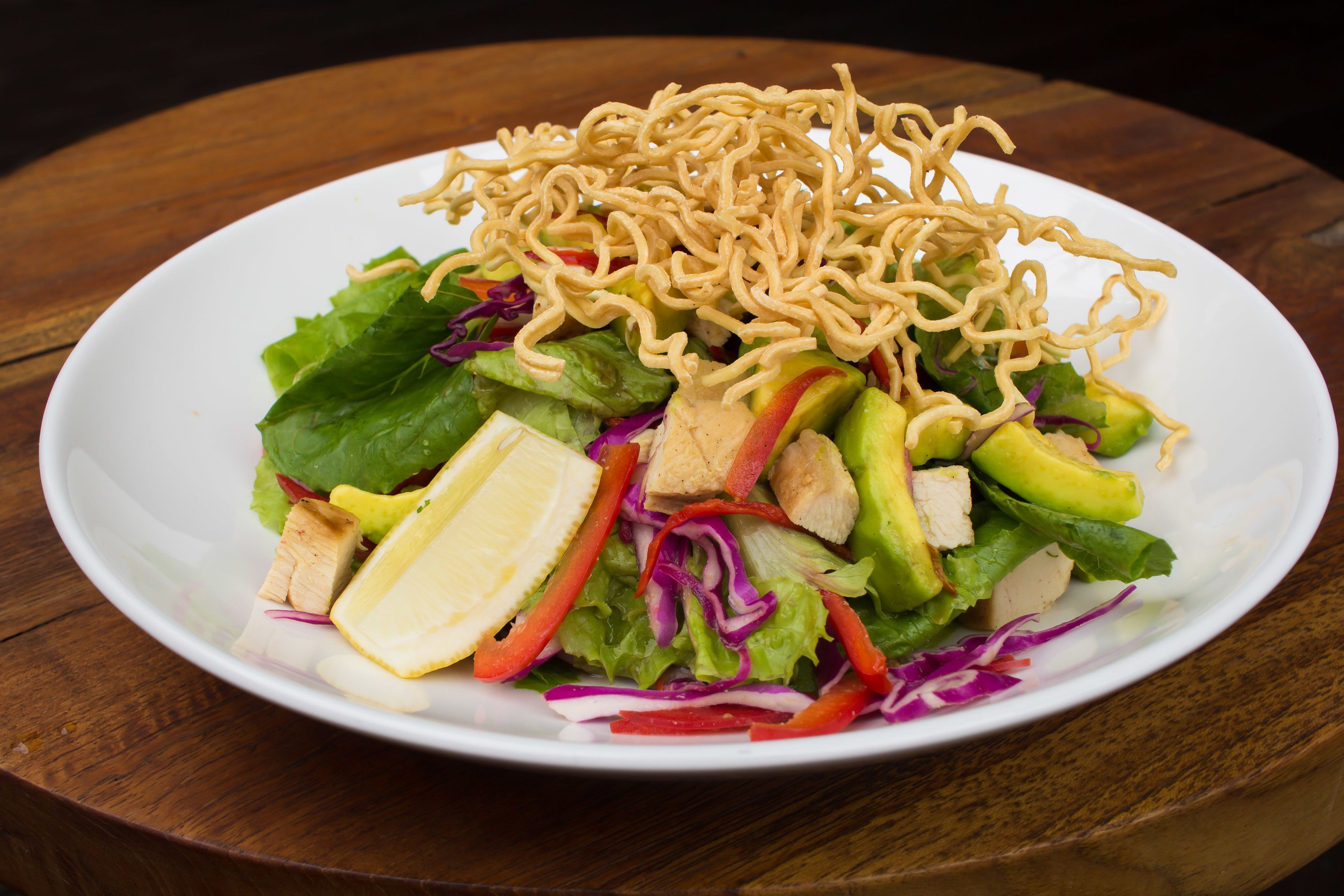 A plate of salad with various vegetables and noodles on a wooden table.