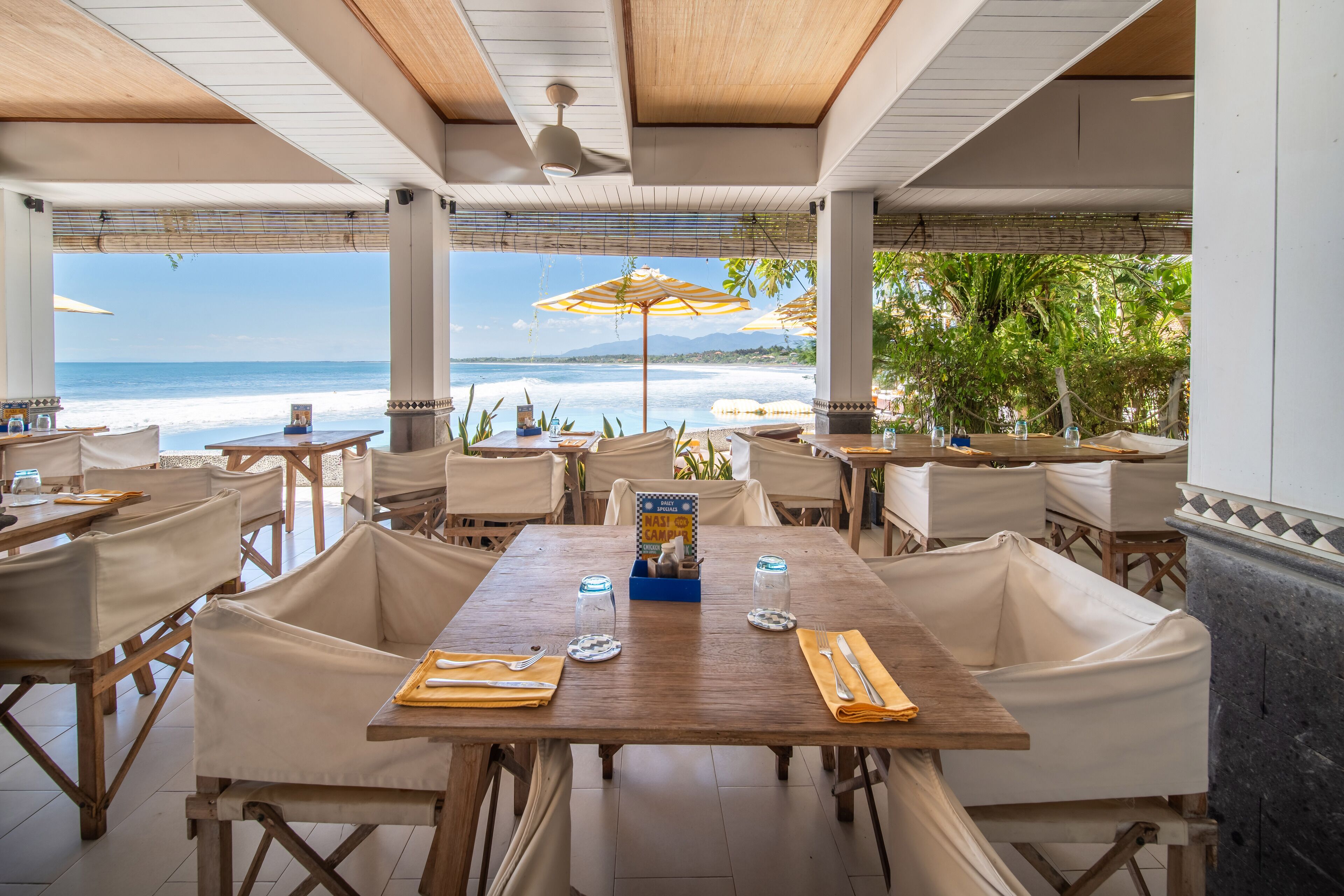 A beachside restaurant with tables and chairs, a view of the ocean, and umbrellas.