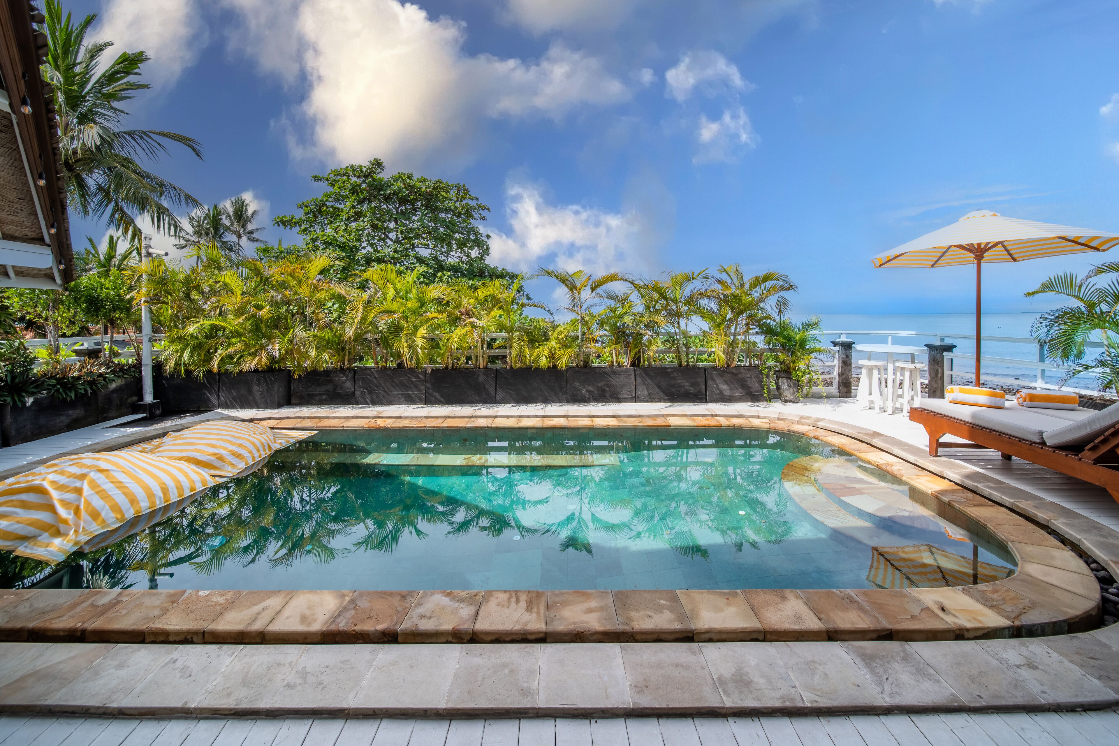 A swimming pool with a curved edge, surrounded by palm trees and a view of the ocean.