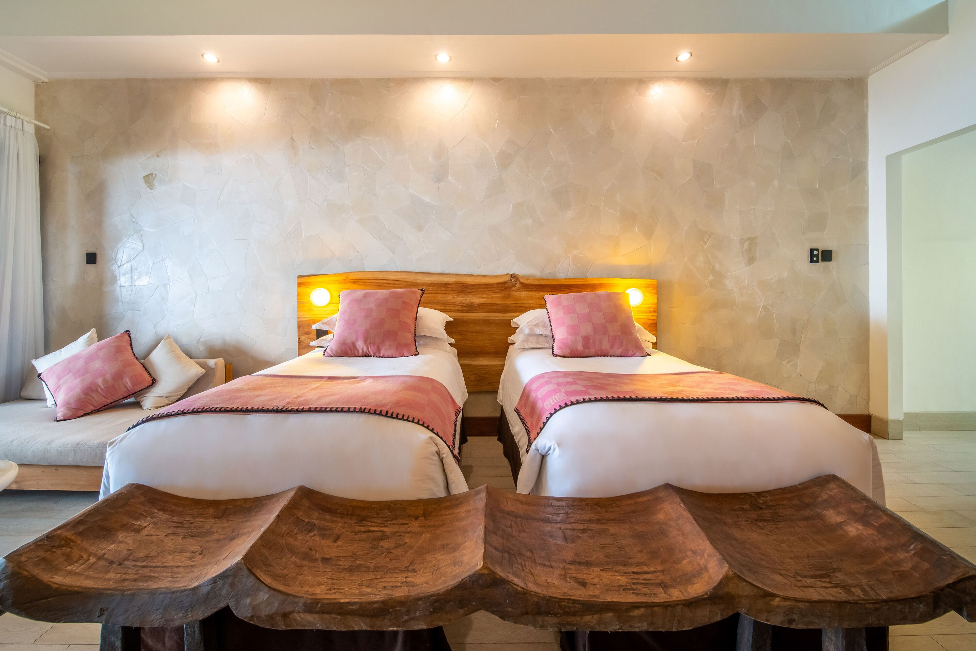 Una habitación doble con dos camas, un banco de madera y una pared de piedra.