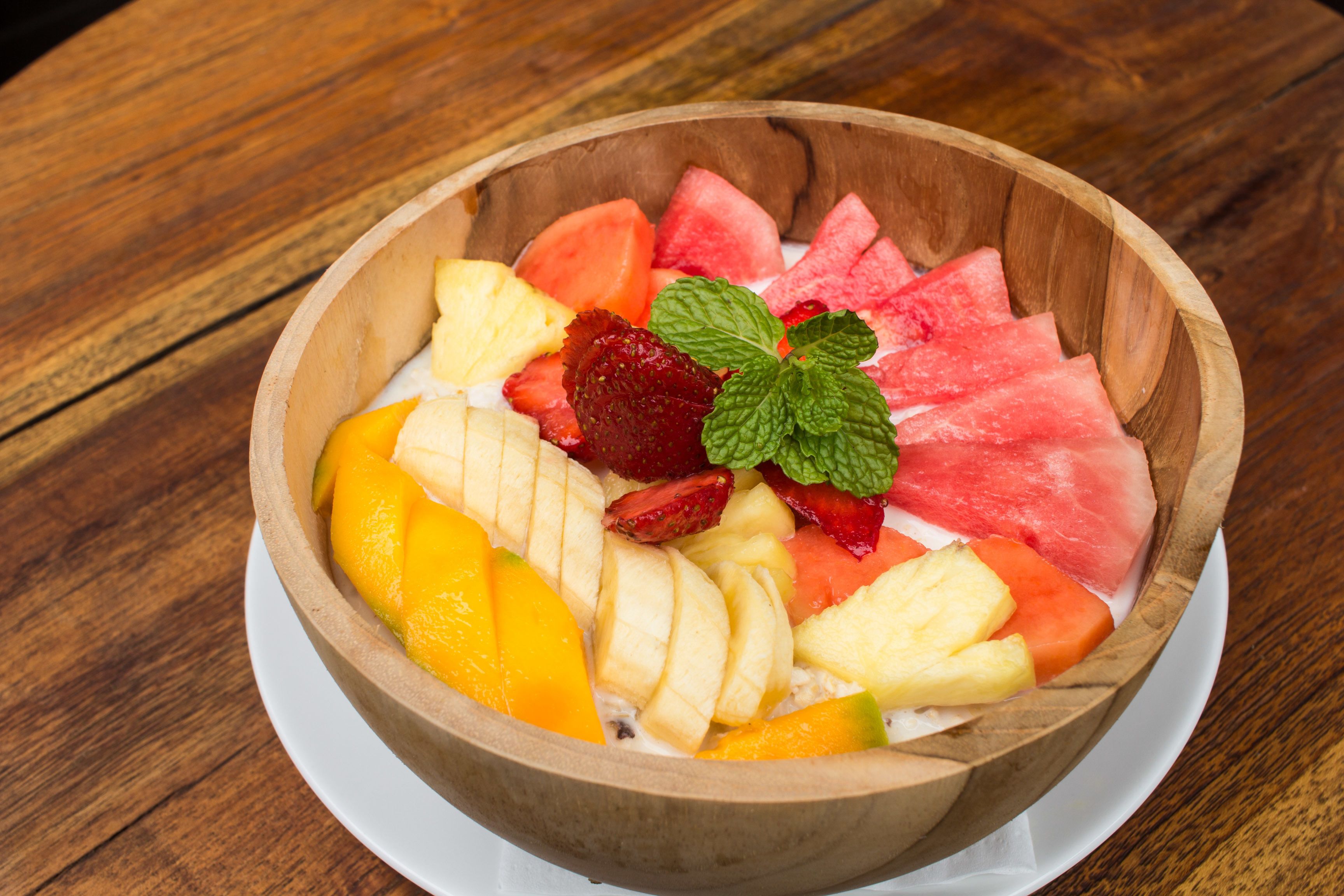 Uma tigela de madeira cheia de frutas fatiadas e uma folha de hortelã sobre uma mesa de madeira.