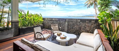 A covered outdoor seating area with a stone wall, wooden furniture, and hanging plants.