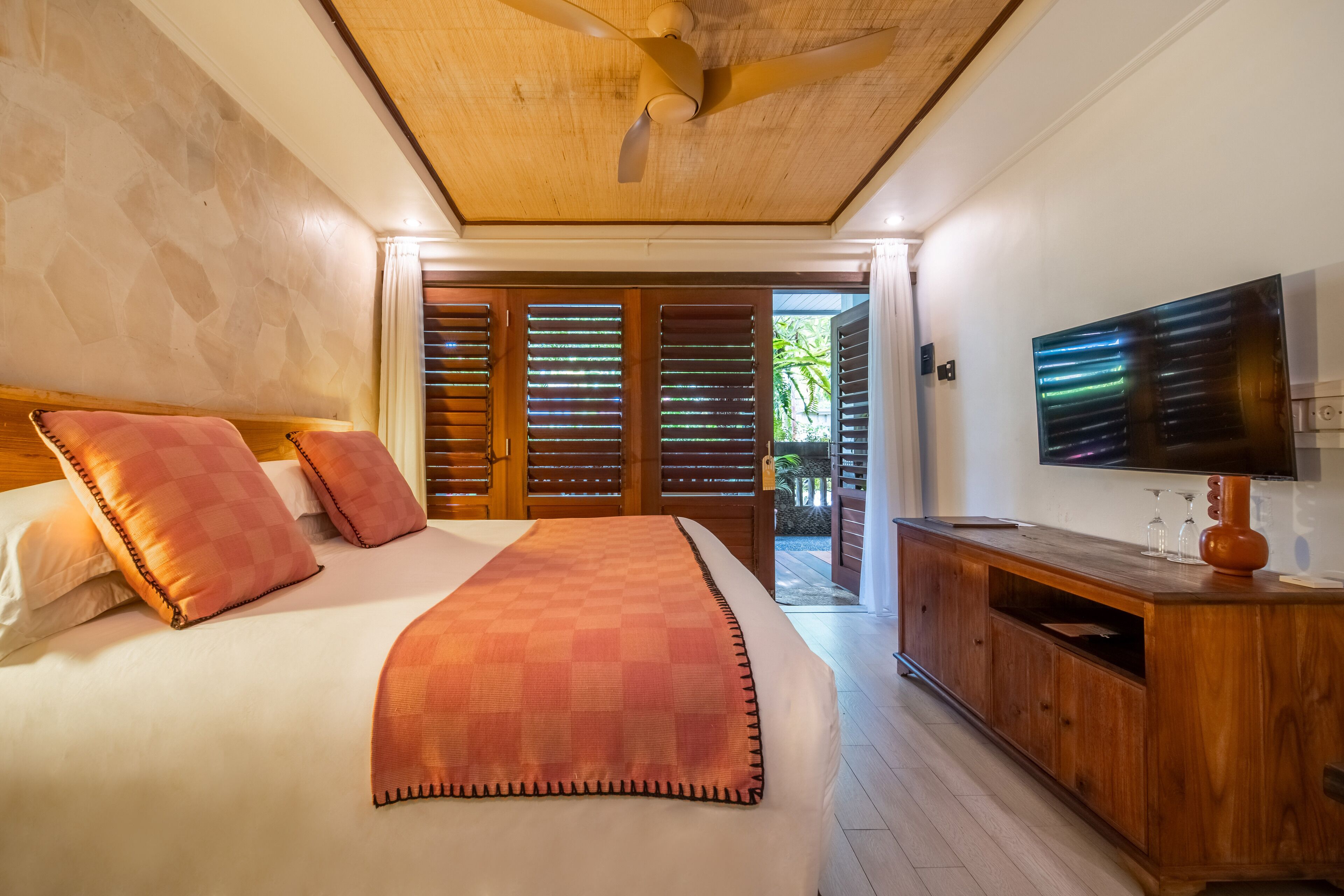 Een slaapkamer met een bed, een houten hoofdbord, een plafondventilator, een televisie en een houten kast.