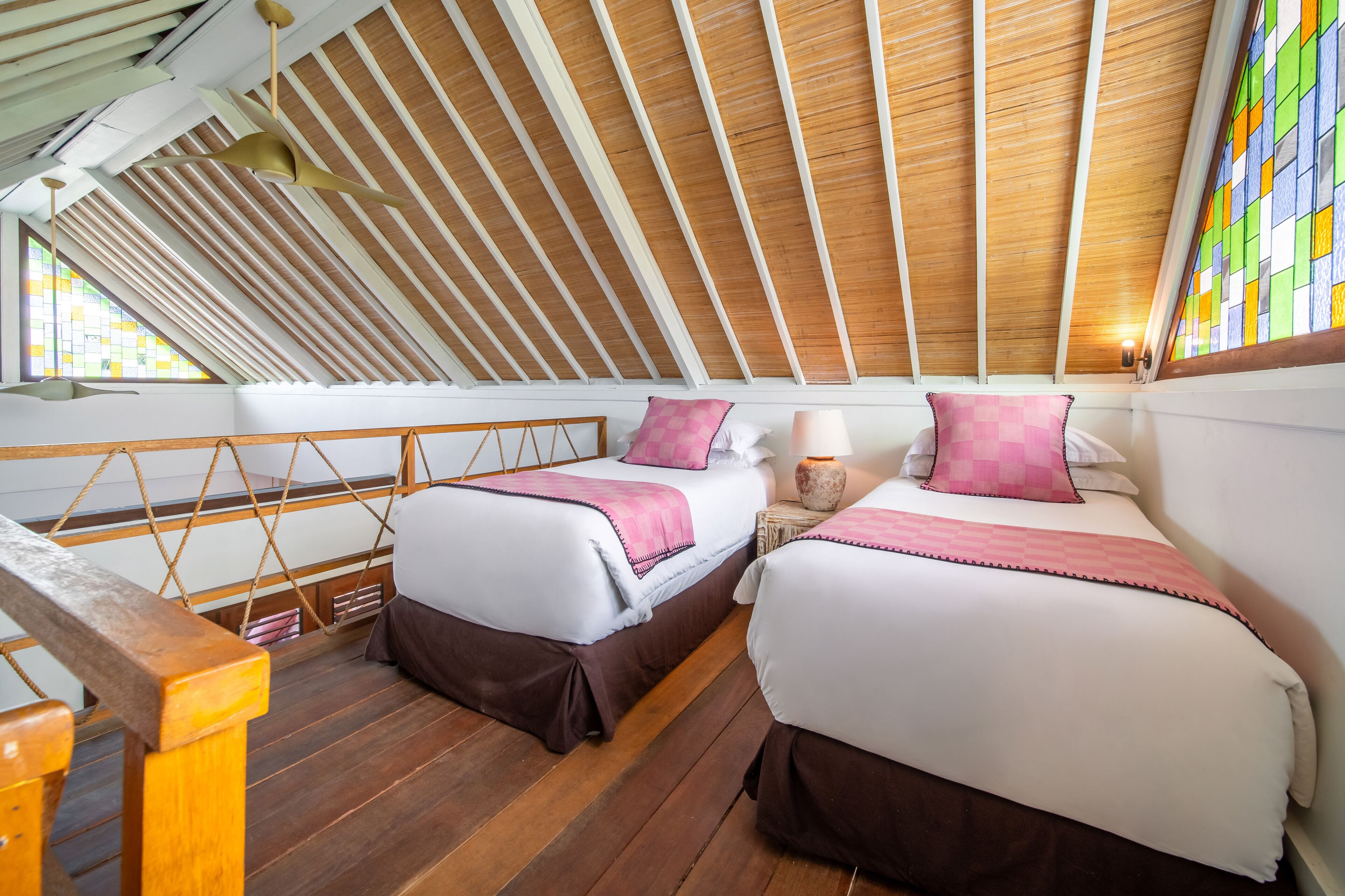 A bedroom with two beds, wooden ceiling beams, and a window with colorful stained glass.